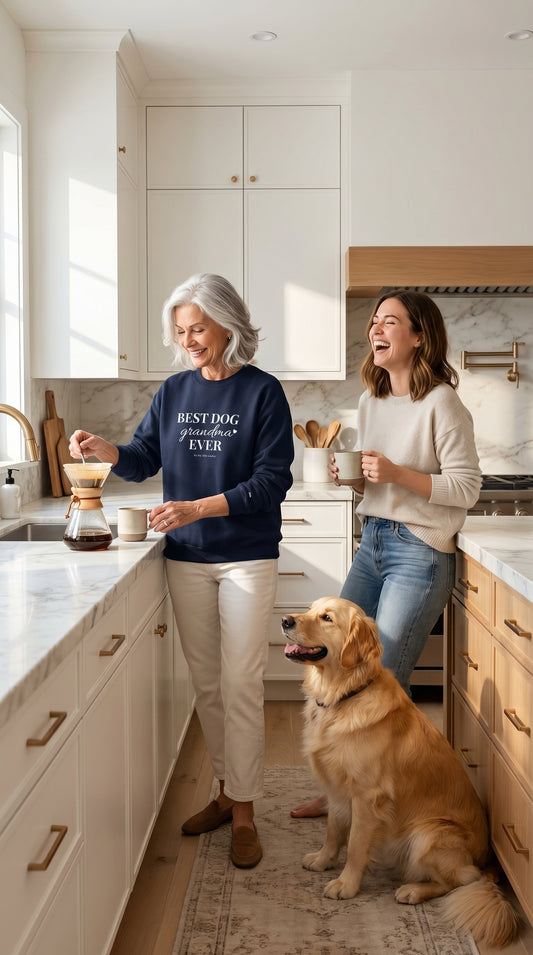 Older woman wearing a Best Dog Grandma crewneck making coffee in a bright kitchen beside a younger woman and a dog in a warm morning setting.