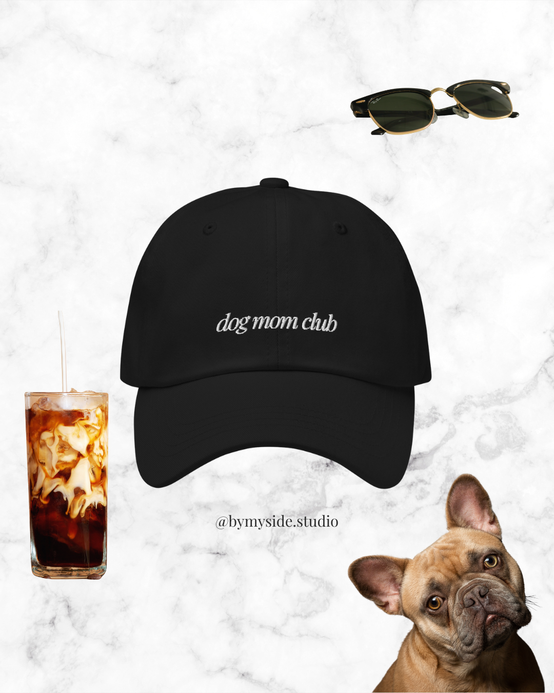 Black baseball cap with 'dog mom club' text, sunglasses, iced coffee, and a French bulldog on a marble background.