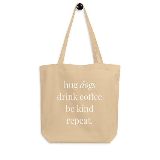 Beige tote bag with text 'hug dogs drink coffee be kind repeat.' on a white background