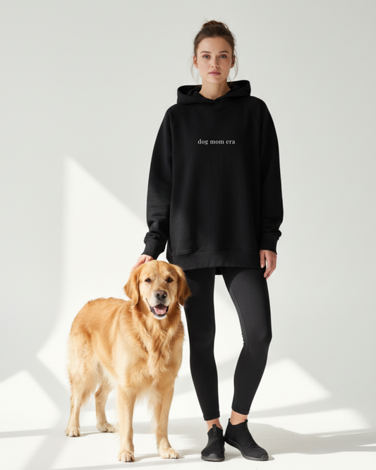 Woman wearing a black hoodie with 'dog mom era' text standing next to a golden retriever on a white background