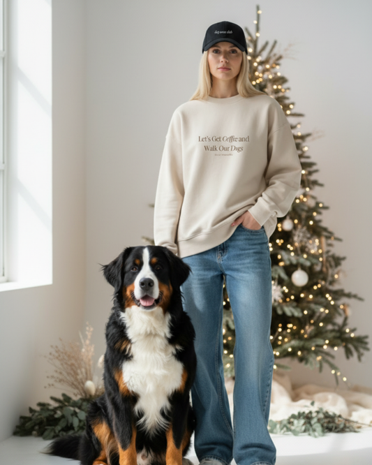 Person wearing a beige sweatshirt with text, standing next to a dog in a room with a Christmas tree. Let’s Get Coffee /  Embroidered - Crewneck