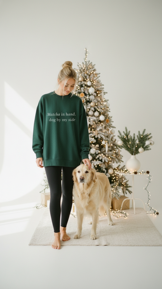 Woman in green sweatshirt and black leggings standing next to a golden retriever in a room with Christmas decorations.
