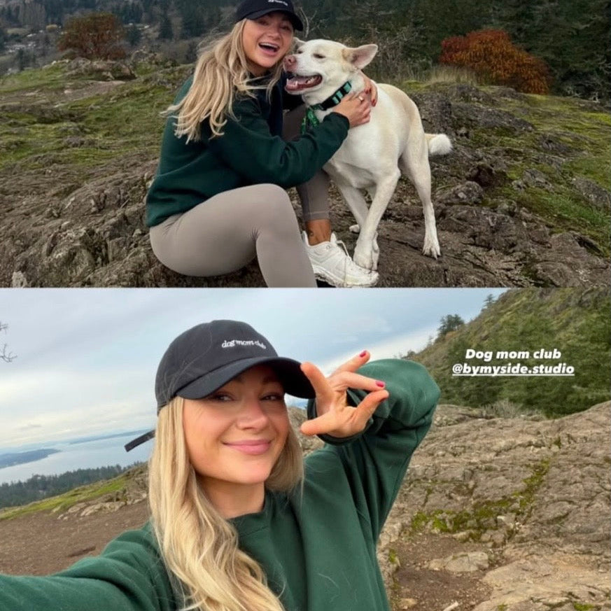 Woman with a white dog on a rocky hillside, with a scenic background wearing Dog Mom Club baseball cap