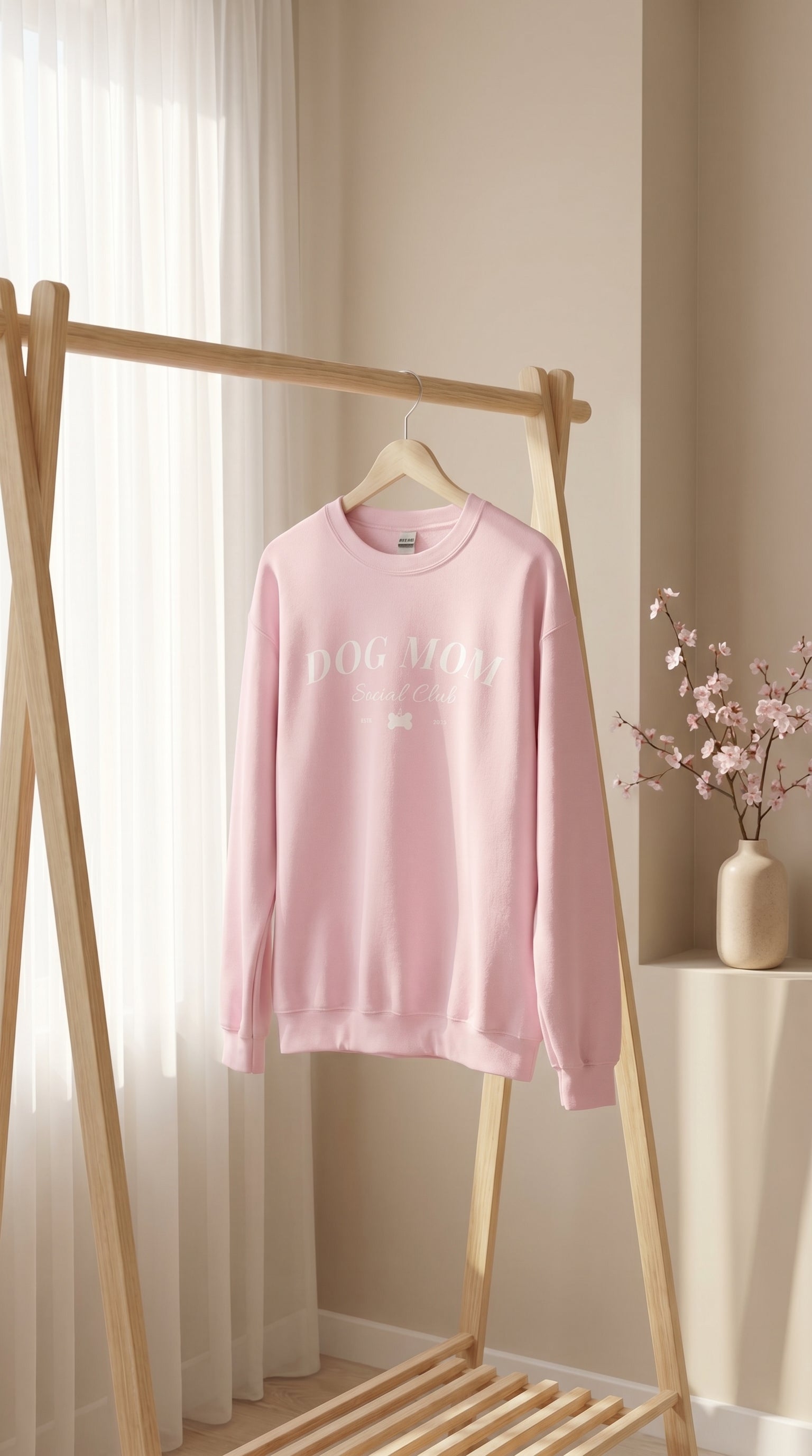 Pink sweatshirt with text on a wooden rack against a neutral wall.