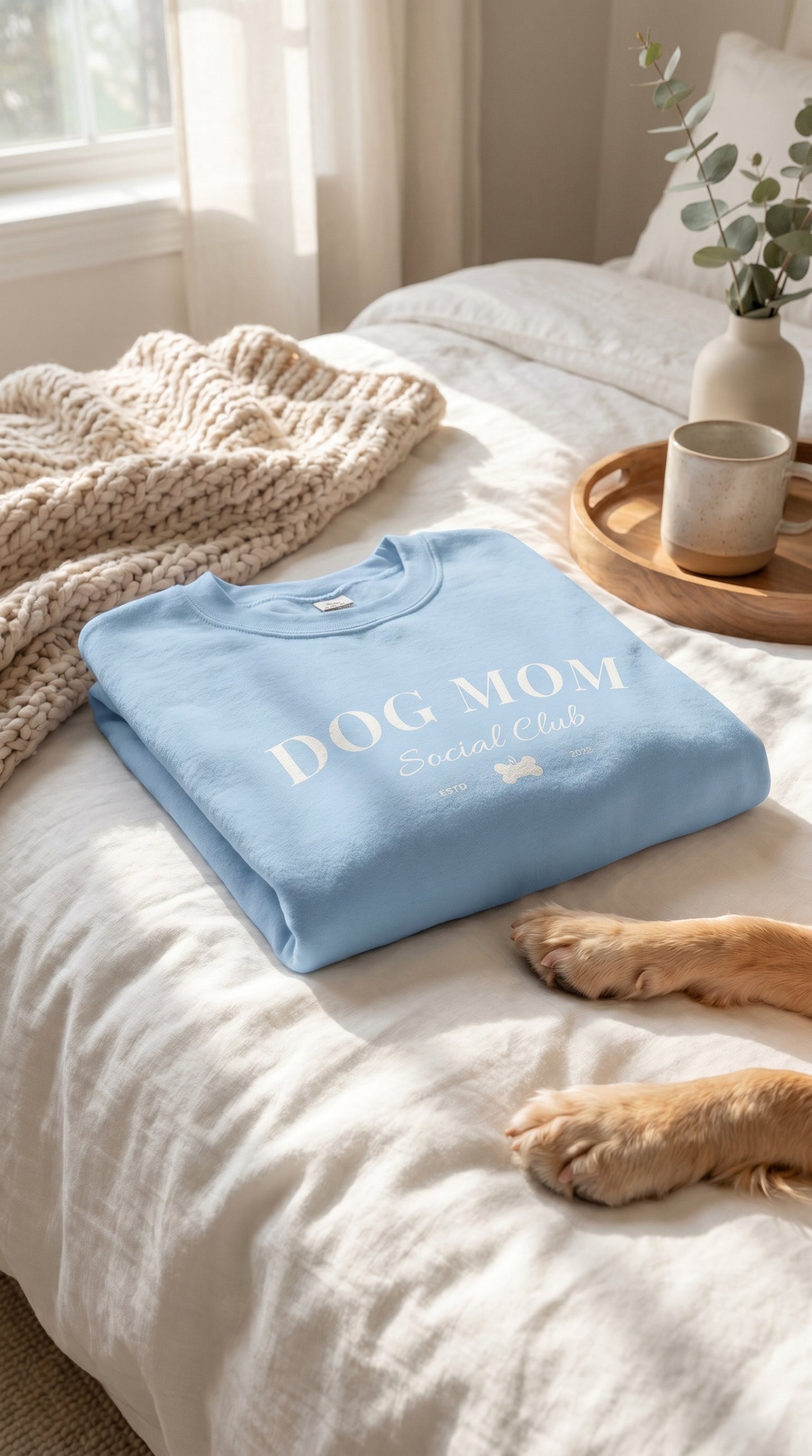 Folded blue towel with 'DOG MOM' text on a bed with a dog's paw visible