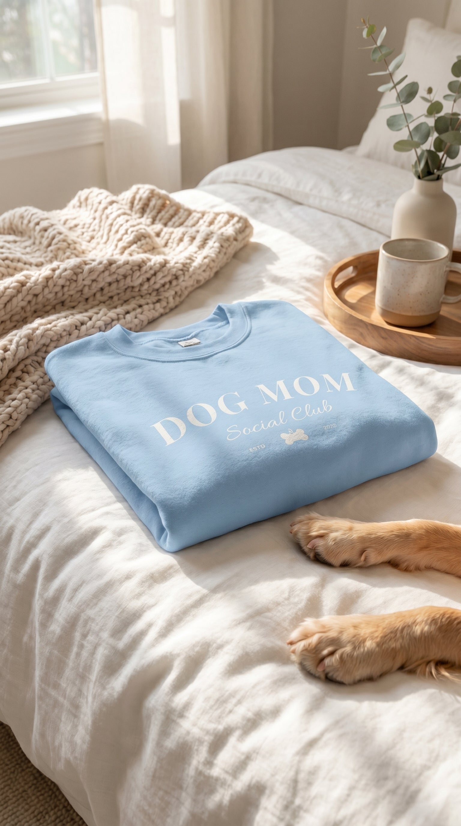 Folded blue towel with 'DOG MOM' text on a bed with a dog's paw visible