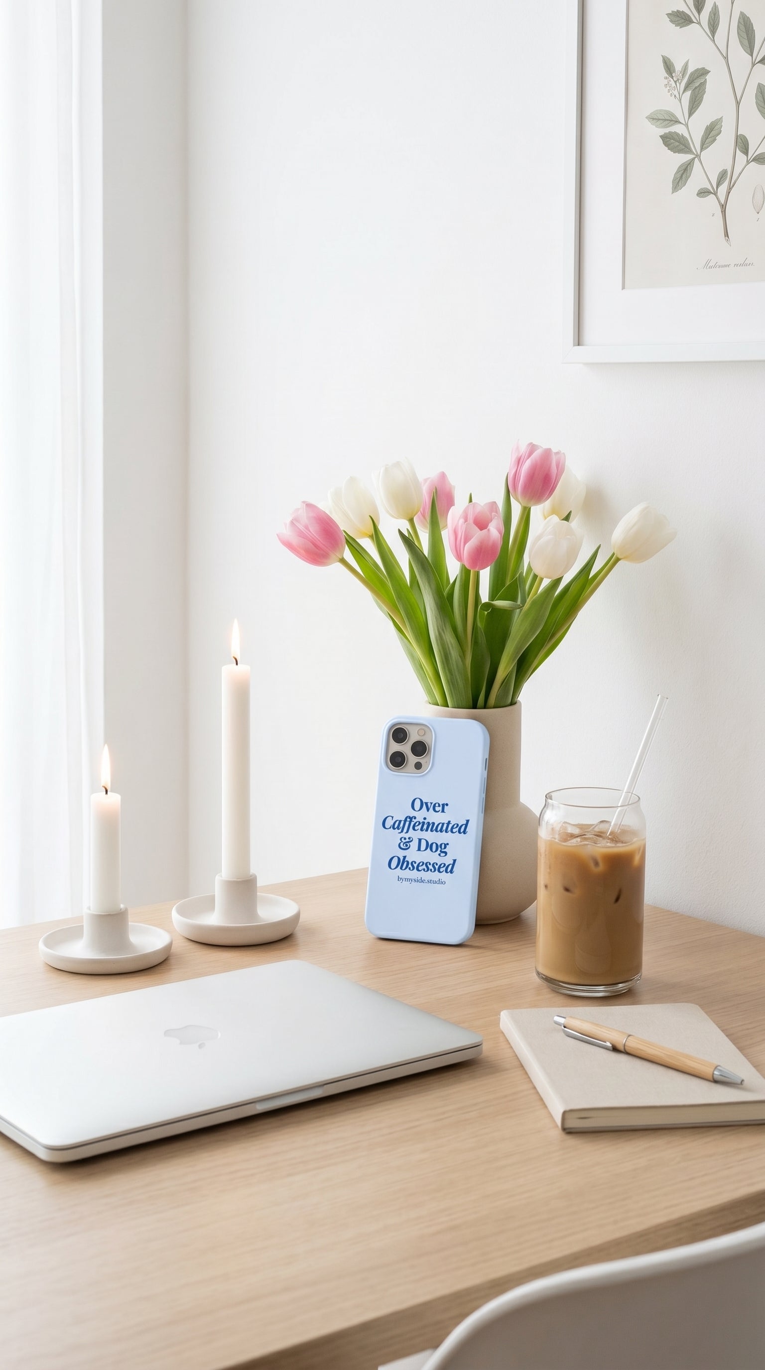 Minimal desk setup featuring a pastel blue dog mom iPhone case, iced coffee, tulips, and neutral decor.