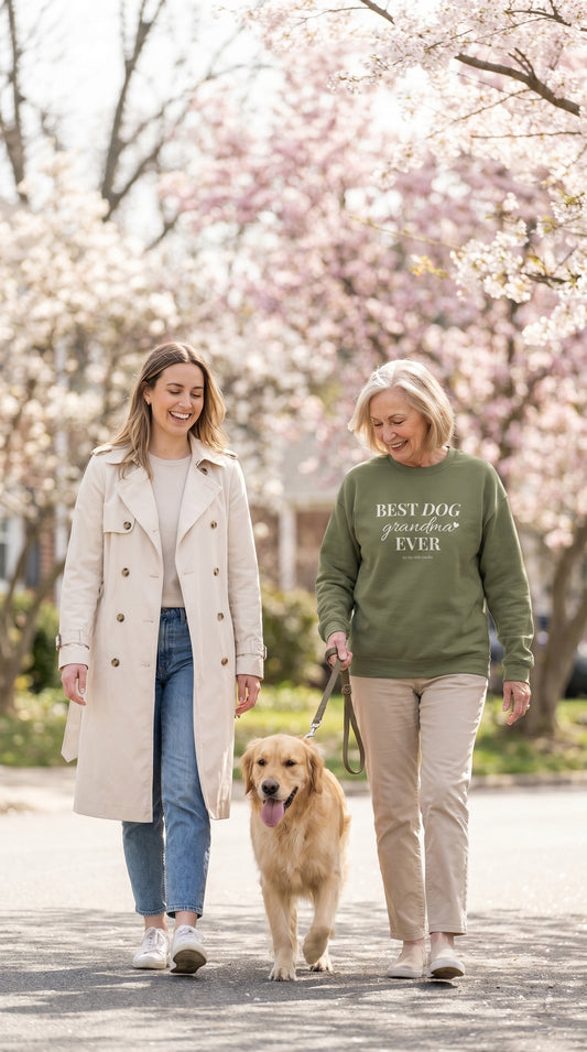 Older woman in a Best Dog Grandma crewneck walking outdoors with a younger woman and a happy dog during a bright spring afternoon.