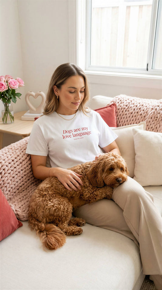 Woman sitting on a couch with a dog, wearing a white t-shirt with text, in a cozy living room.