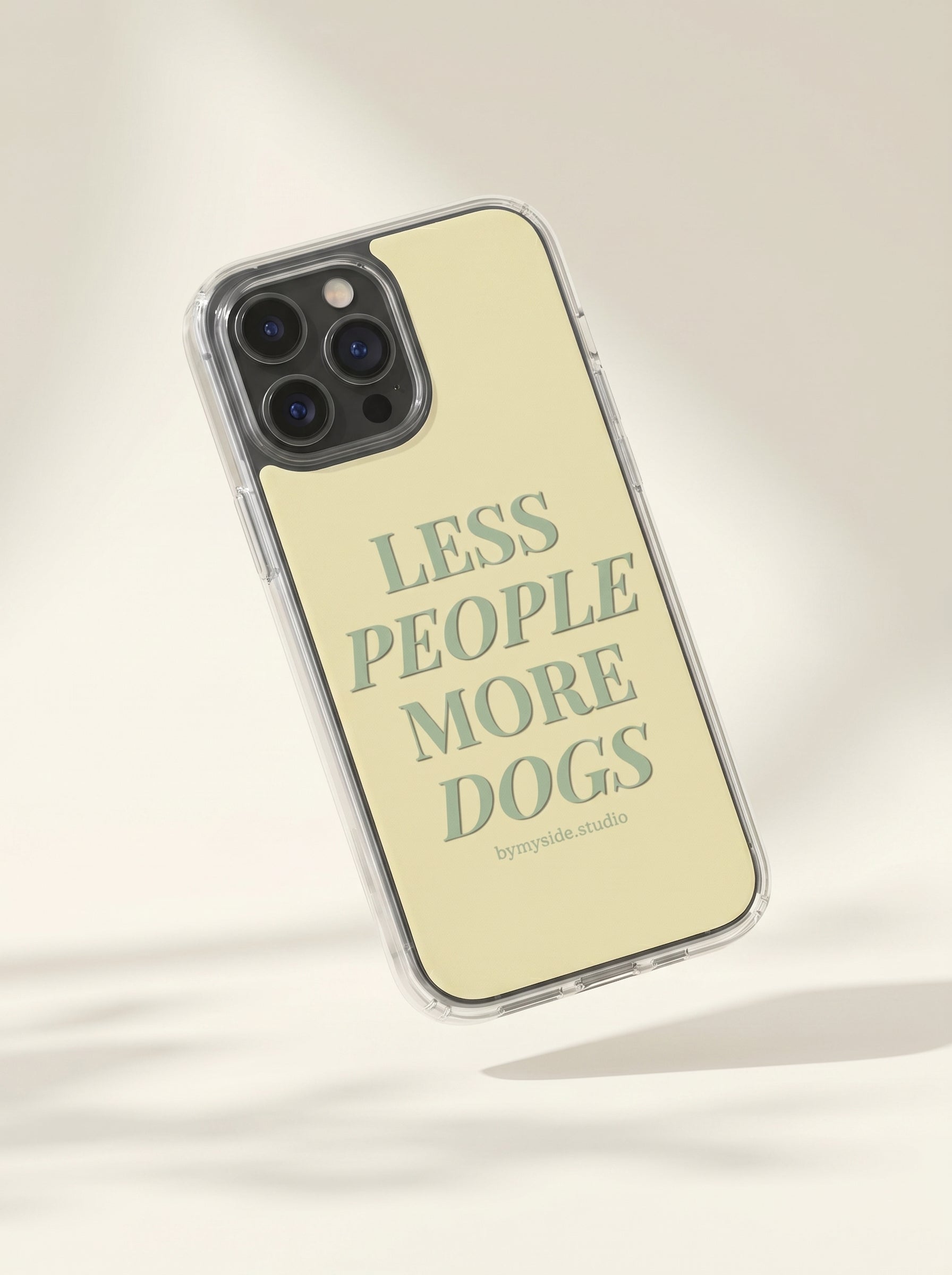 Minimal studio mockup of a pastel yellow “Less People More Dogs” iPhone case on a soft cream background.