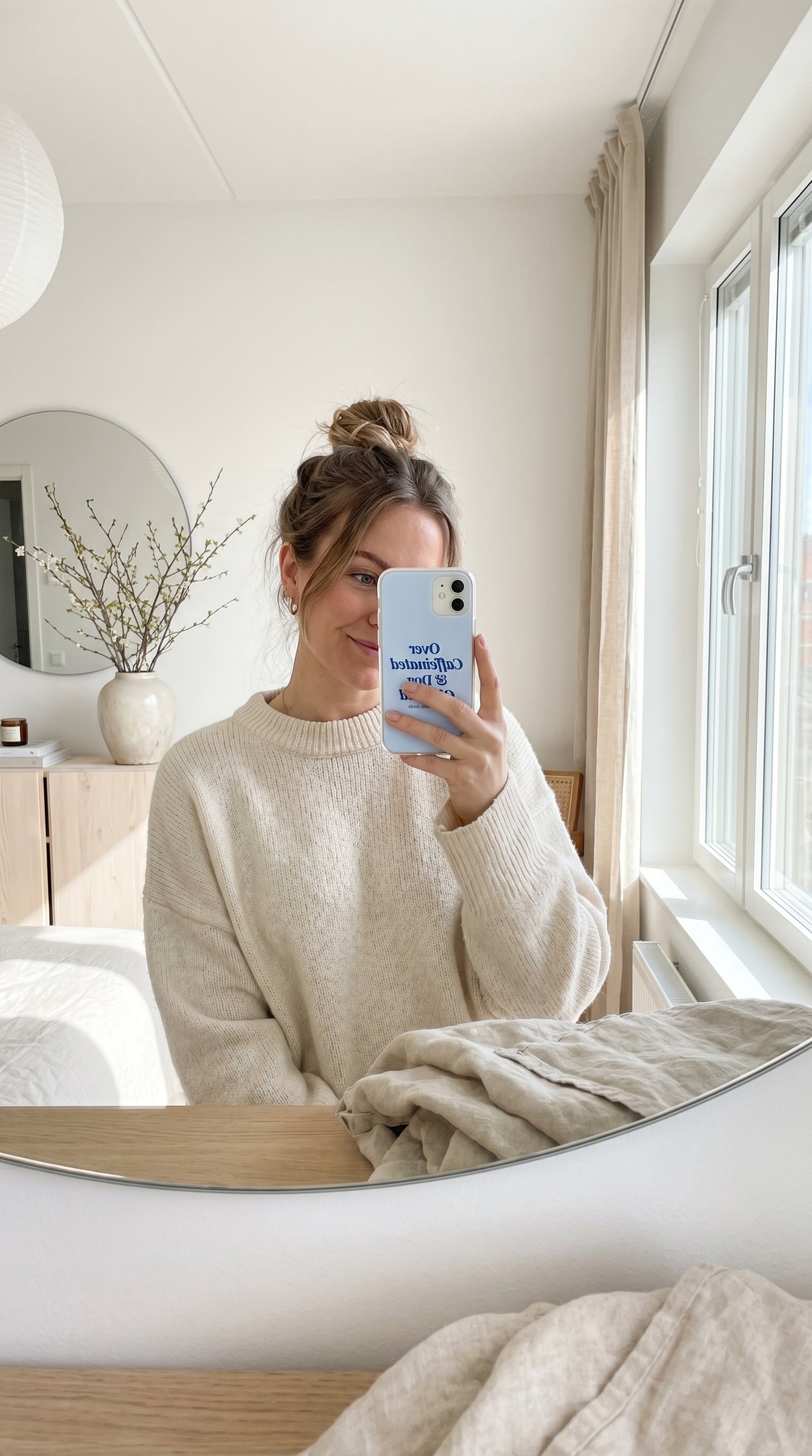 Mirror selfie featuring a pastel blue “Over Caffeinated & Dog Obsessed” iPhone case in a bright neutral apartment.