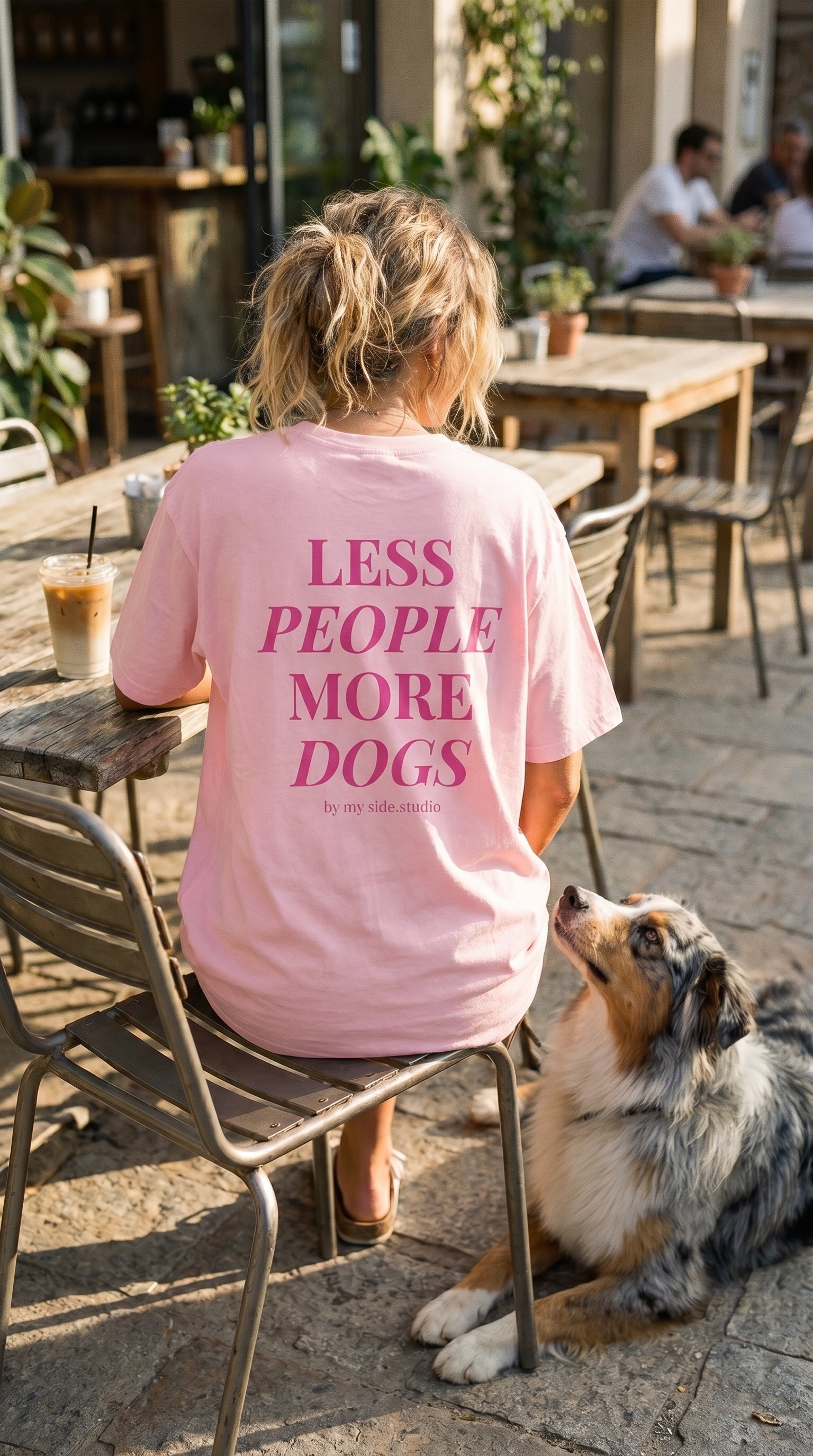 Person wearing a pink t-shirt with 'LESS PEOPLE MORE DOGS' text, sitting outdoors with a dog.