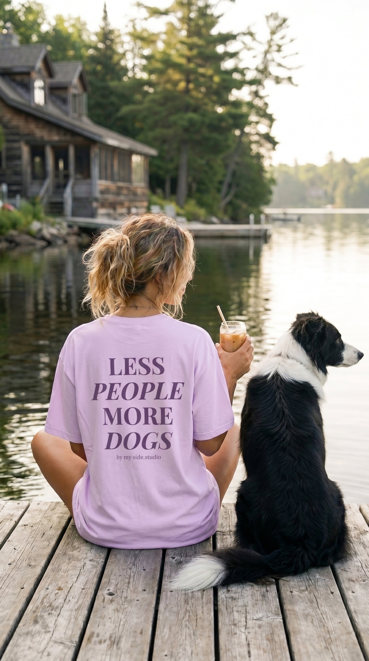 Person wearing a 'LESS PEOPLE MORE DOGS' shirt sitting on a dock with a dog, enjoying a drink.