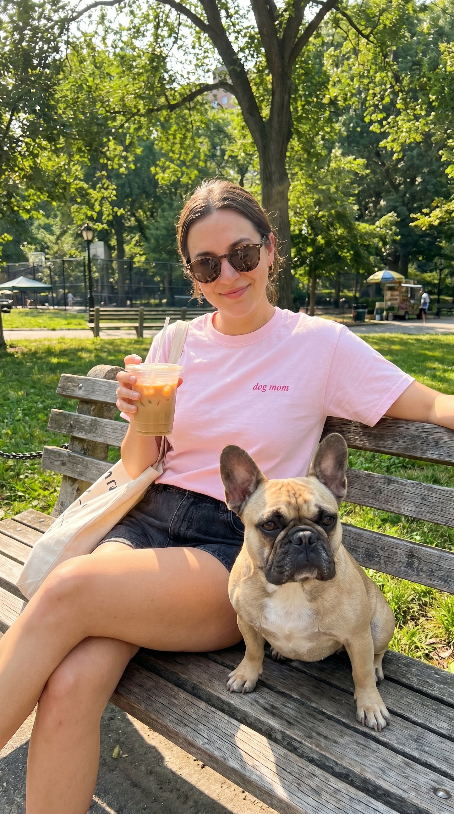 Woman sitting on a park bench with a dog, holding a drink.