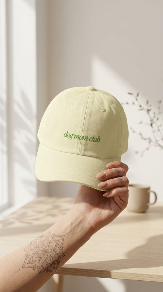 Light green cap with 'dogmum club' text held by a hand on a wooden surface.