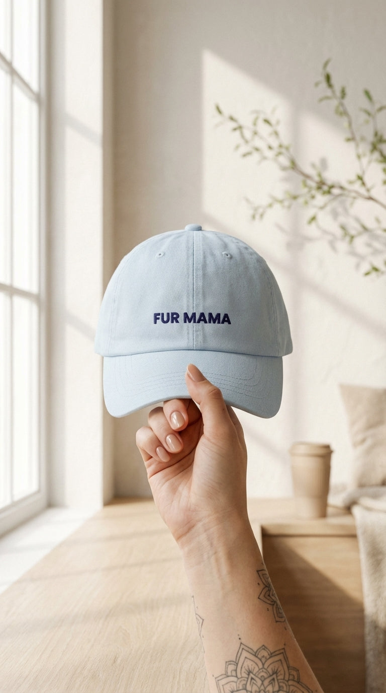 Light blue cap with 'FUR MAMA' text held by a hand in a bright room.