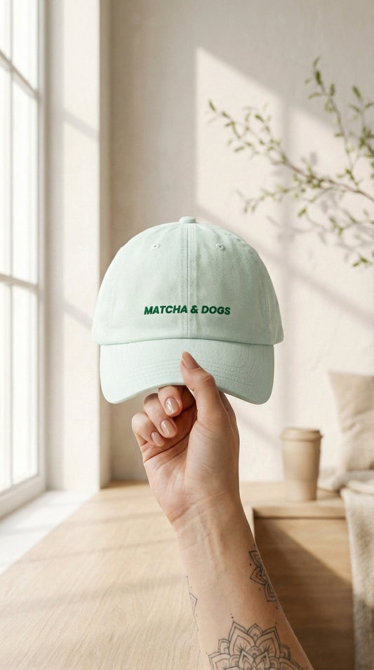 Light green cap with 'Matcha & Dogs' text held by a hand in a bright room.