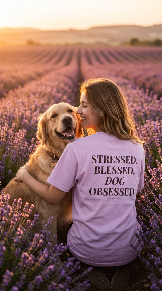 A woman in a lavender field hugging a golden retriever, wearing a light purple t-shirt with the text 'STRESSED, BLESSED, DOG OBSESSED.' printed on the back.