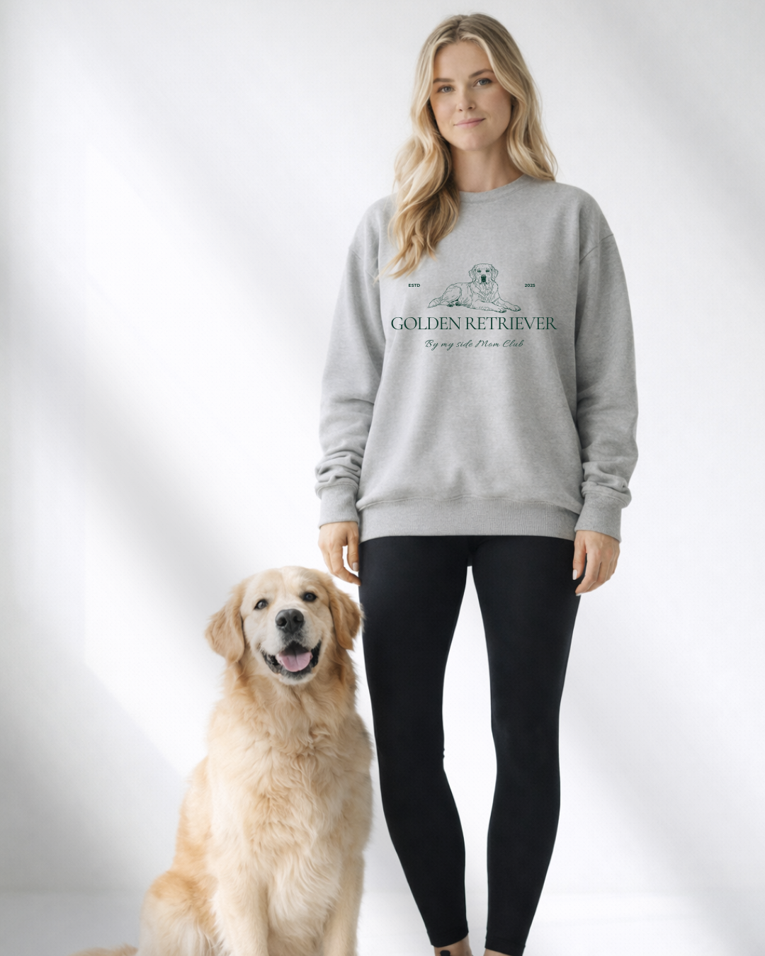 Woman wearing a gray sweatshirt with a Golden Retriever design, standing next to a Golden Retriever dog on a white background.