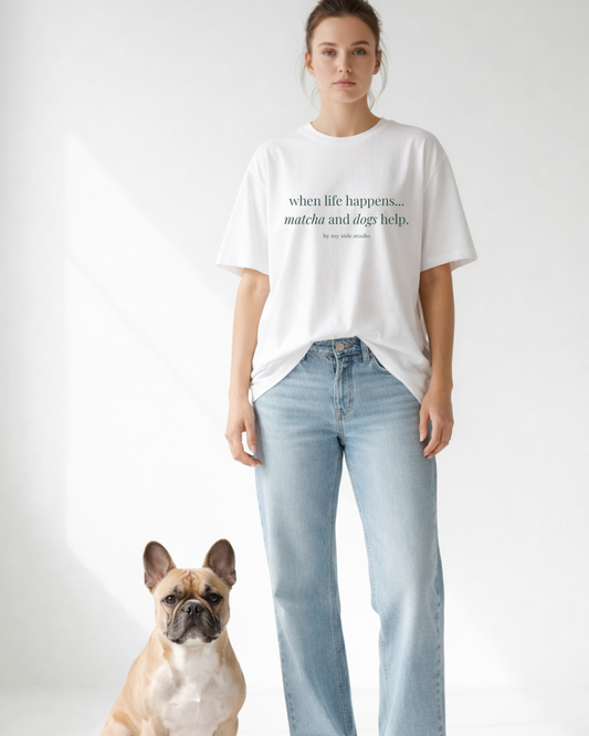 Person wearing a white t-shirt with text and light blue jeans standing next to a dog on a plain background