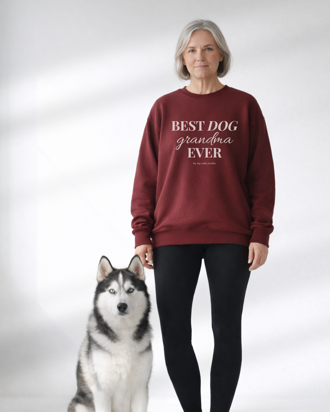 Woman wearing a maroon sweatshirt with 'BEST DOG GRANDMA EVER' text, standing next to a dog on a white background