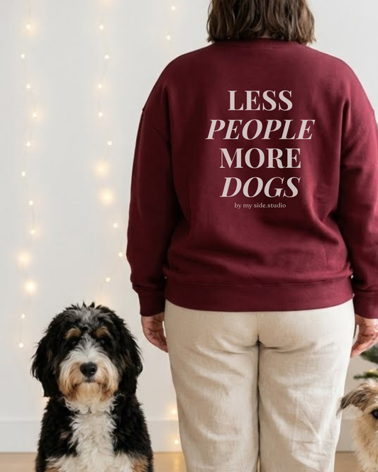 Person wearing a maroon sweatshirt with 'LESS PEOPLE MORE DOGS' text, standing next to a dog indoors.